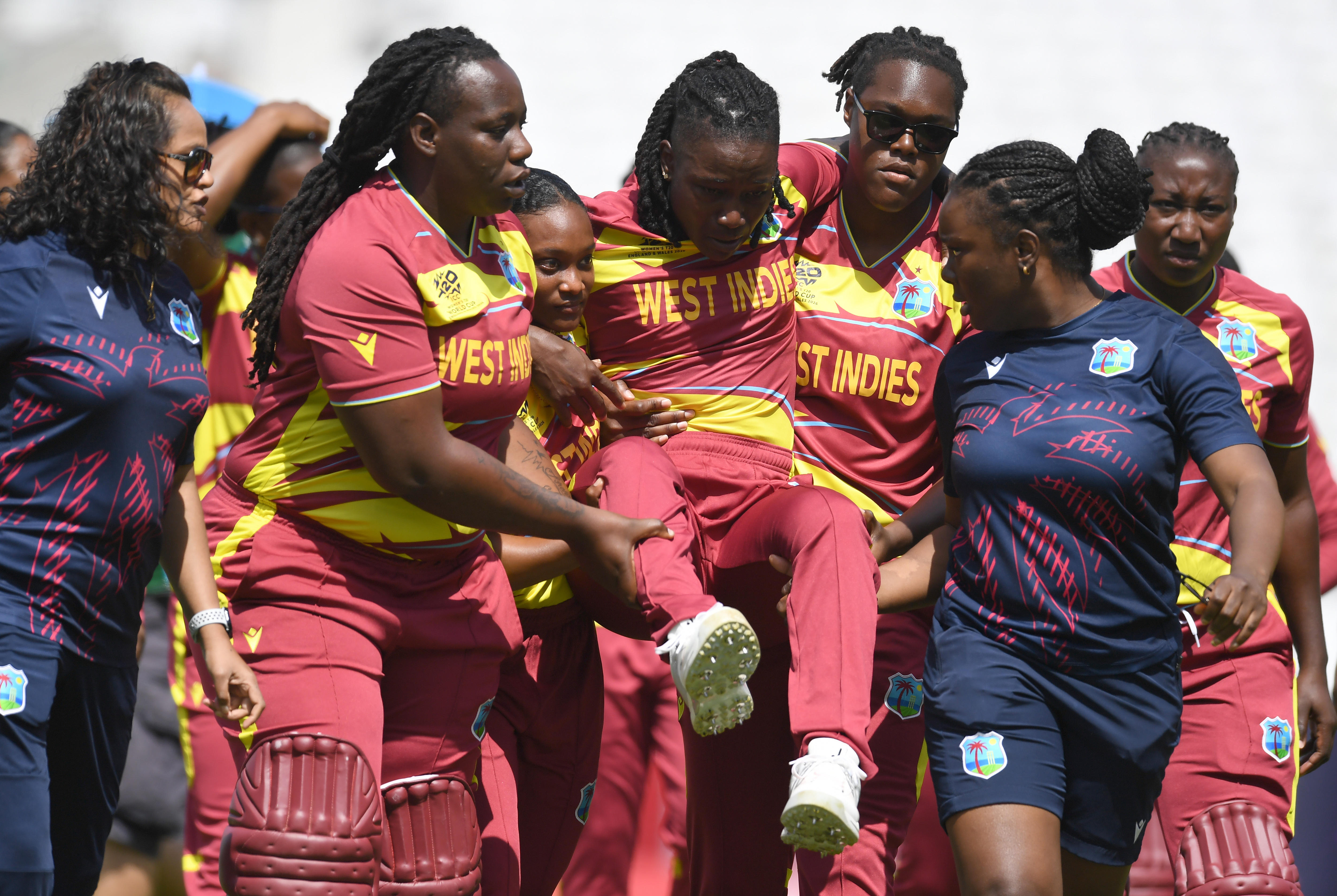 A cricketer is carried off the field by teammates.
