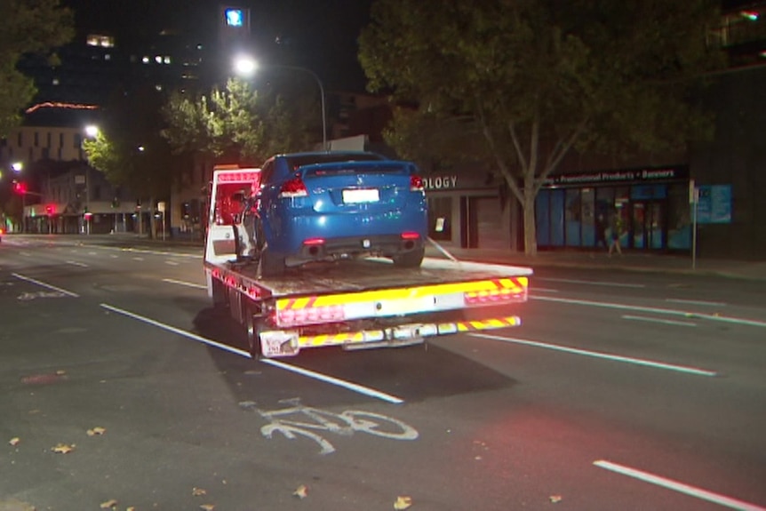 A blue car on the back of a tray truck at night