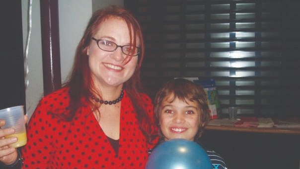 A woman in a red dress stands next to her young son. Both are looking at the camera and smiling.