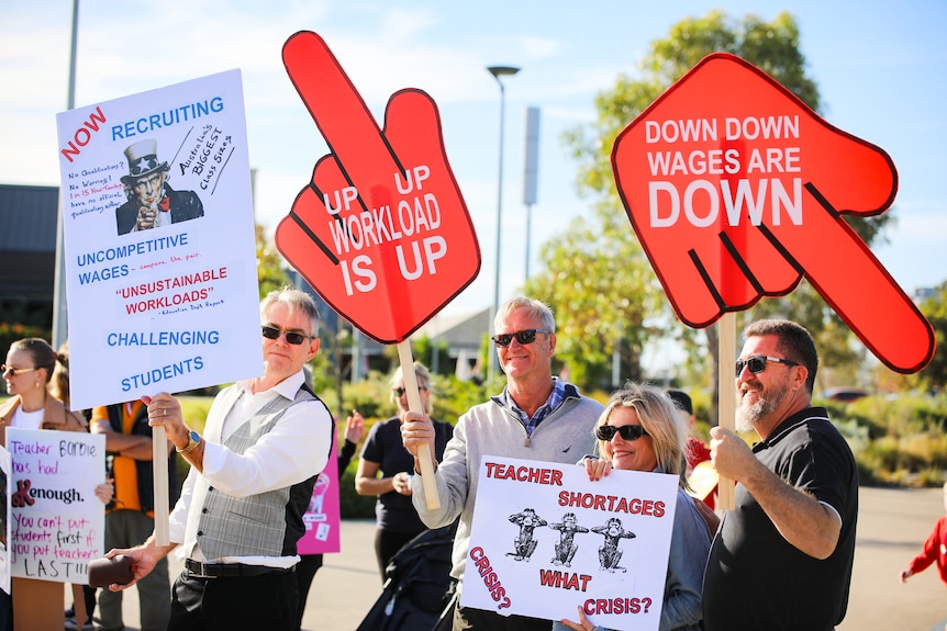 Teachers smiling and holding rally signs at a strike action in Perth.
