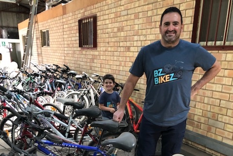 A man smiles for the camera surrounded by bicycles