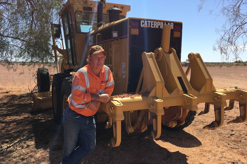 Barry Turner leaning on his new yellow tractor that he uses to manipulate the soil for the EMU project