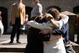 Three women stand outside in a tight embrace