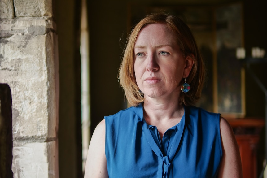 Claire Harris stands next to a stone window looking out. 