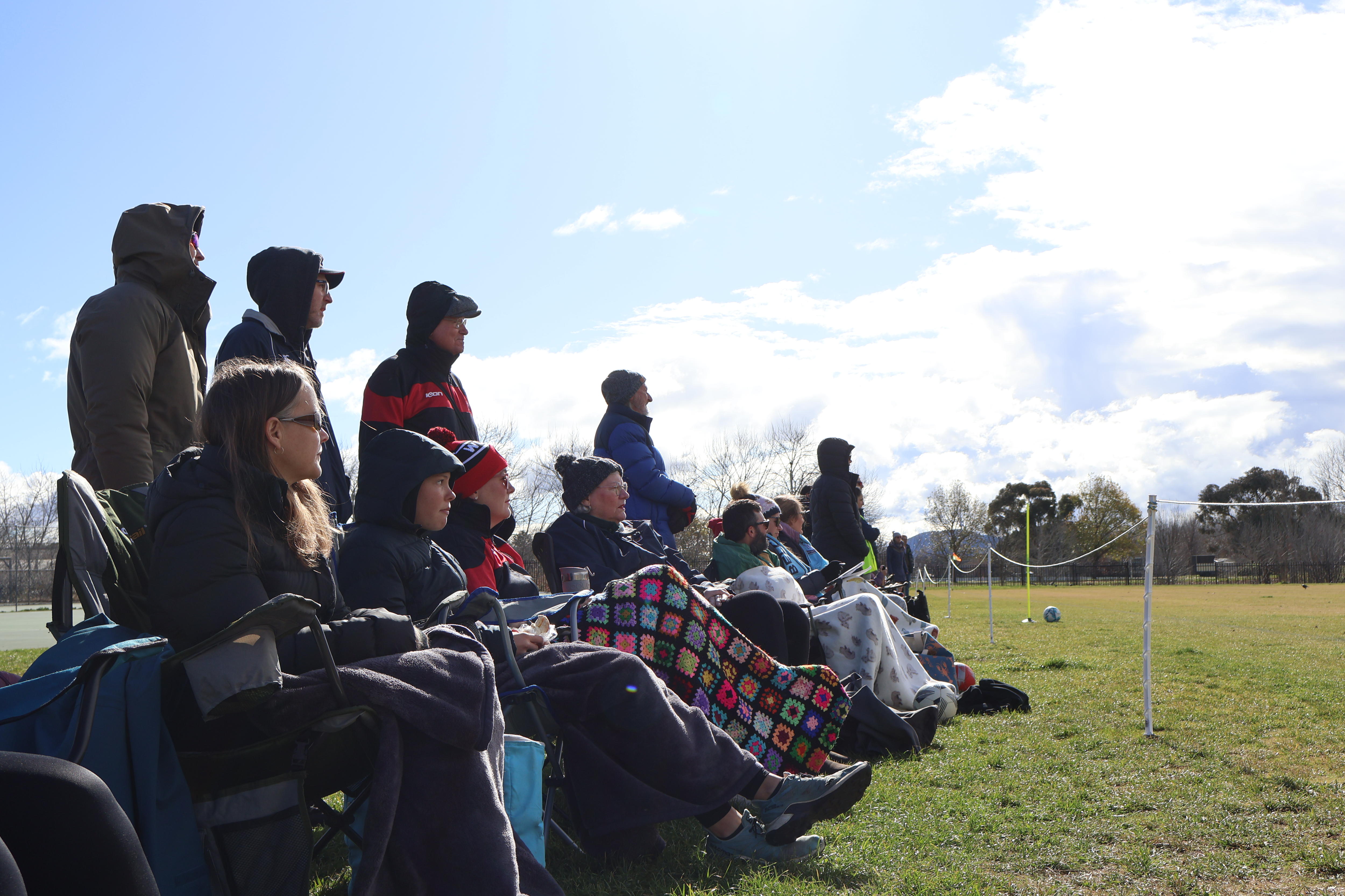 A group of people waiting kids sport sitting on the sidelines. 