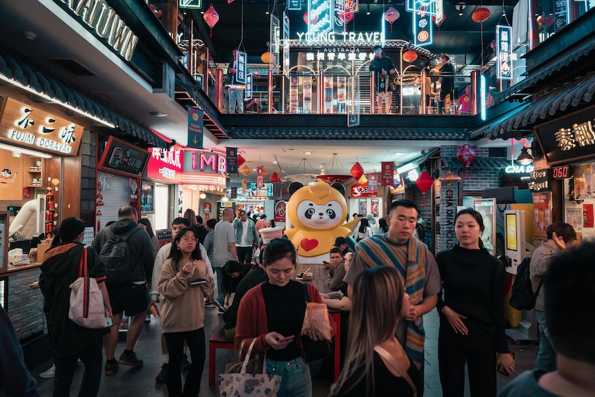 A photo of people walking through a neon sign lit food court in Burwood's Chinatown.