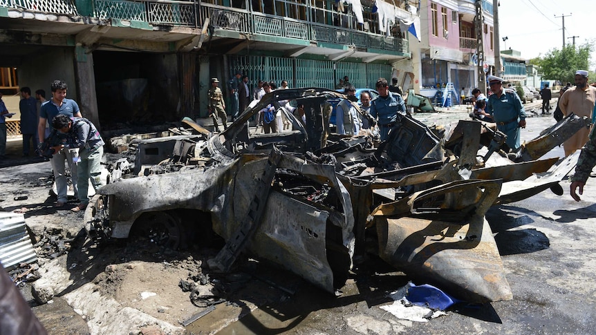 Afghan policemen walk around a destroyed vehicle at the site of a suicide attack in Kabul