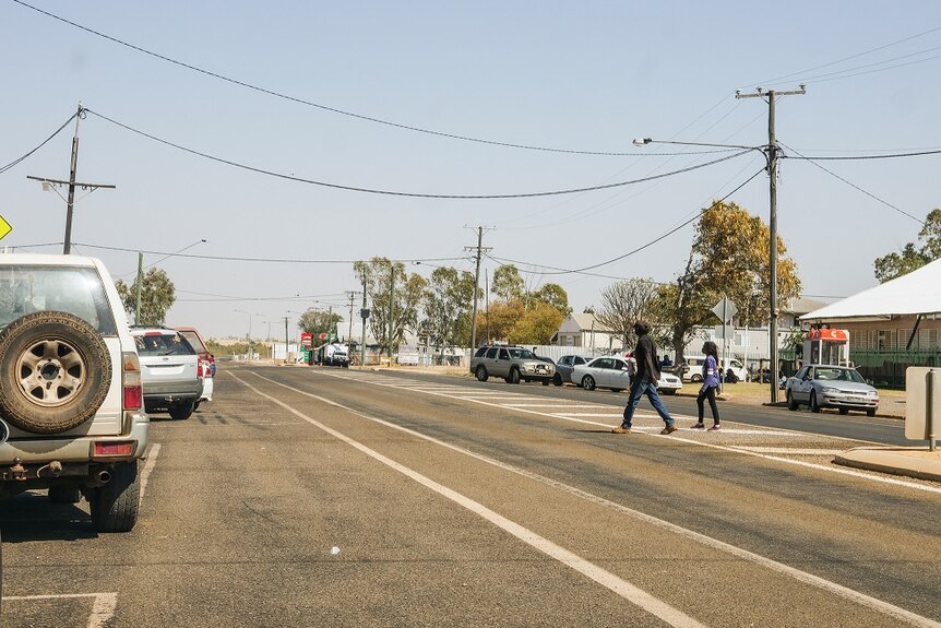 A dusty, rural street with people crossing the road.