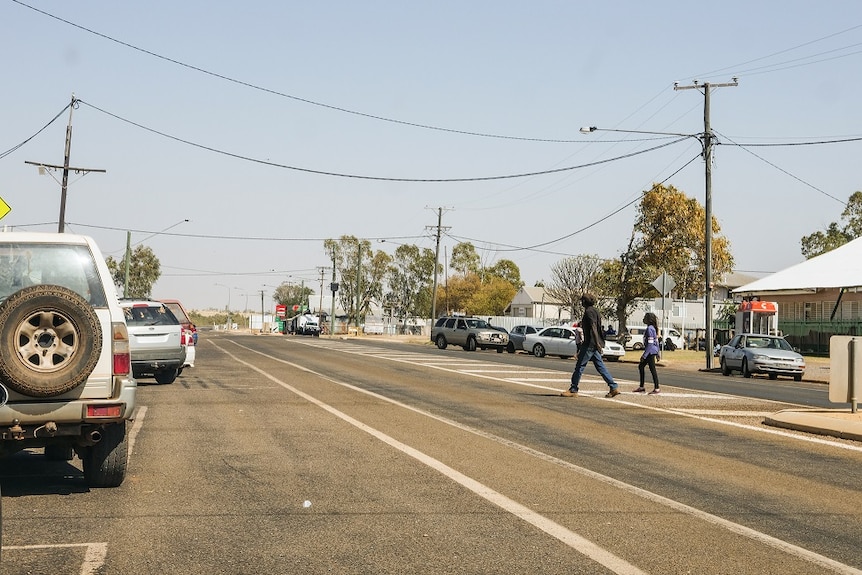 A dusty, rural street with people crossing the road.