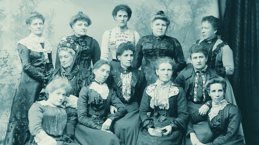 Monochrome studio photo of twelve women in late 19th century clothing.