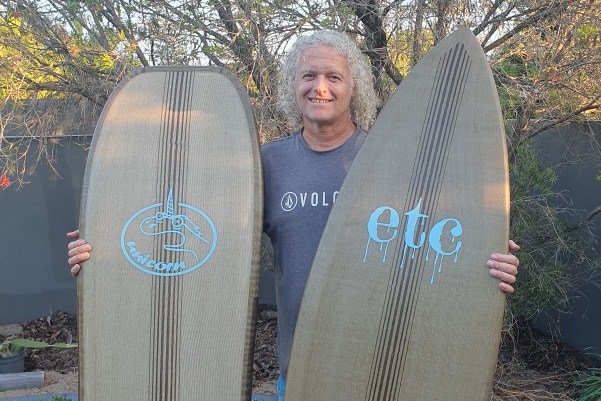 A man holding two surfboards.