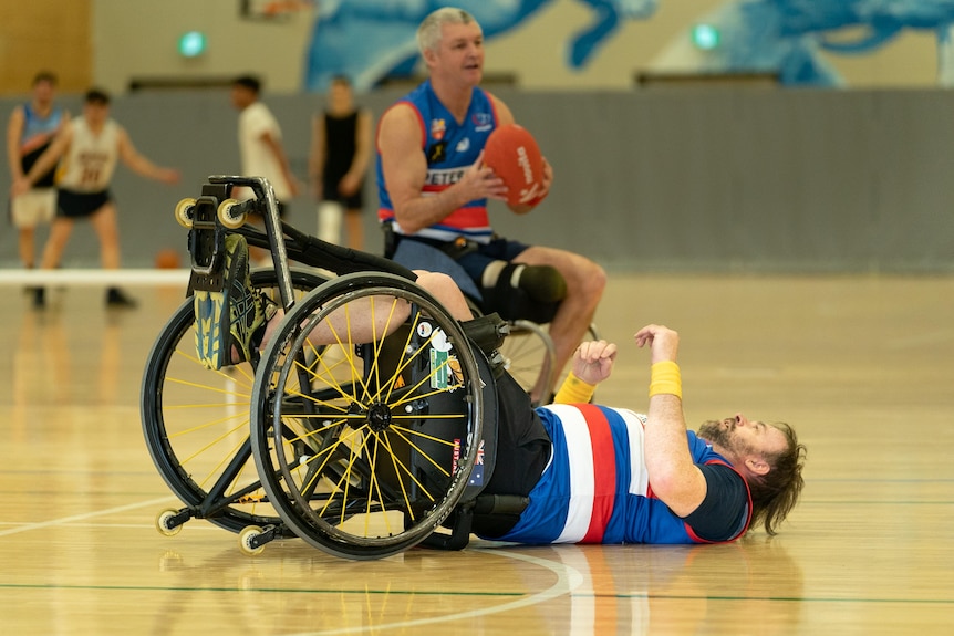 A wheelchair footballer lies on his back on a wooden floor after toppling over in his chair mid-match