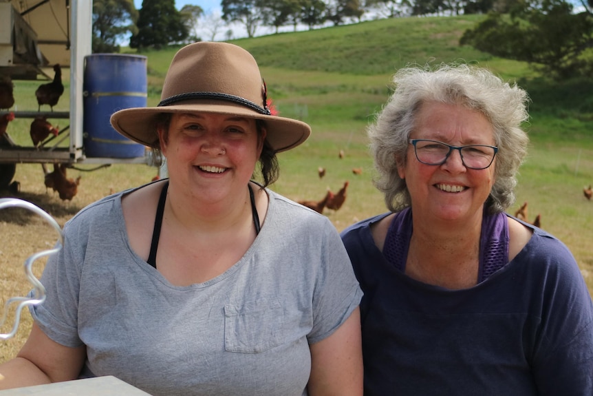 two women stand in a paddock in front of a portable structure housing chickens