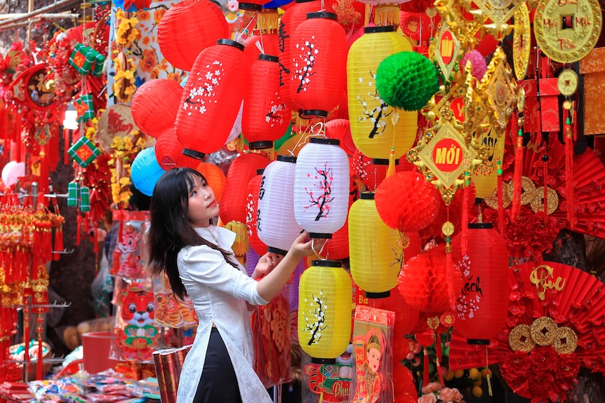 A woman looks at pink, yellow and red lanterns hung at eye level