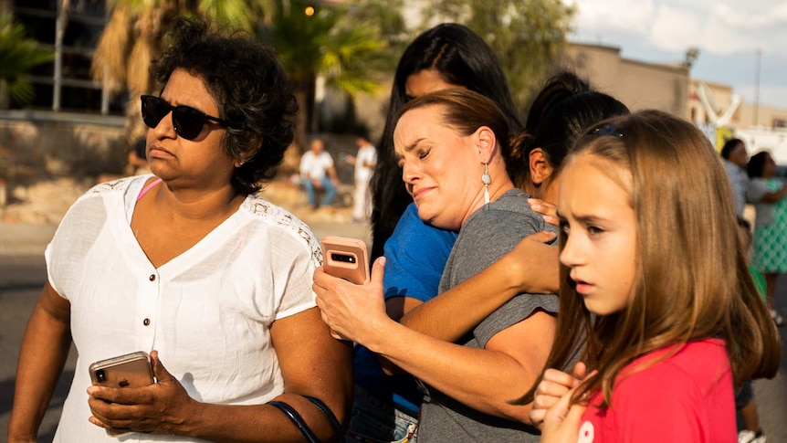 A woman cries while being surrounded by a group of women and girls