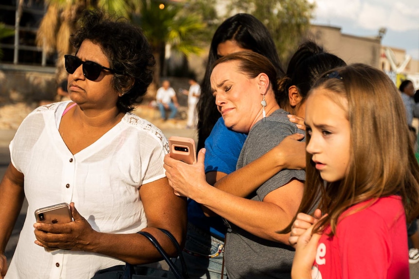 A woman cries while being surrounded by a group of women and girls