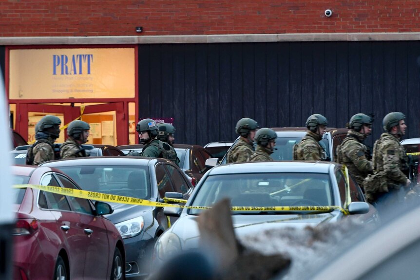 At least 10 police officers seen behind yellow police line and several cars in camouflage gear with helmets.