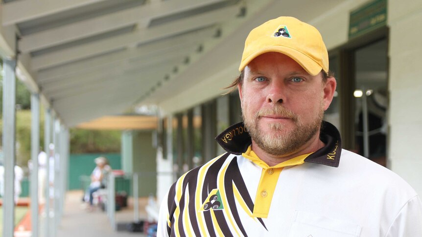 Aaron Freeman looks into the camera wearing his bowling uniform next to the bowling club house.