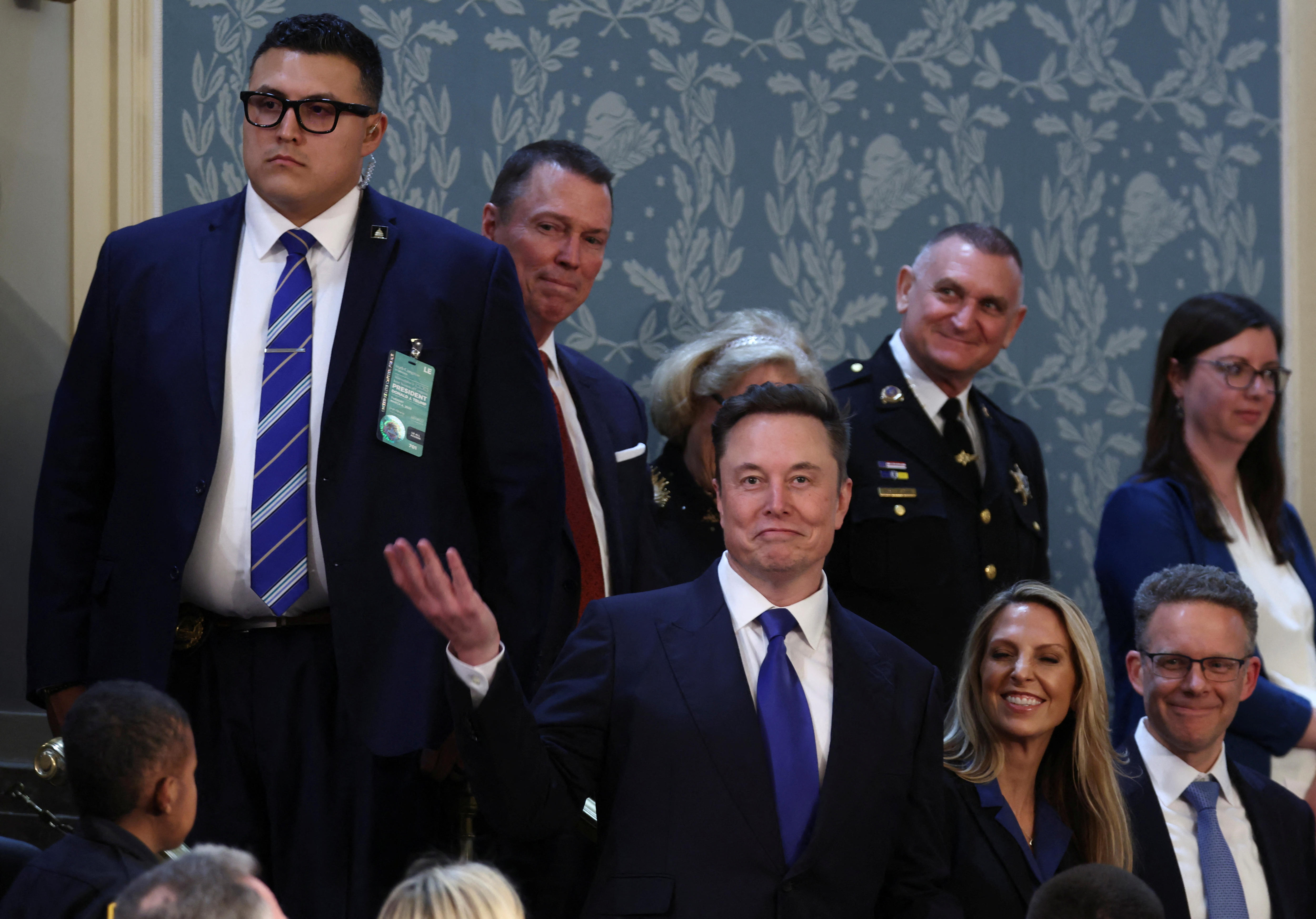 A man in a suit waves coyly 