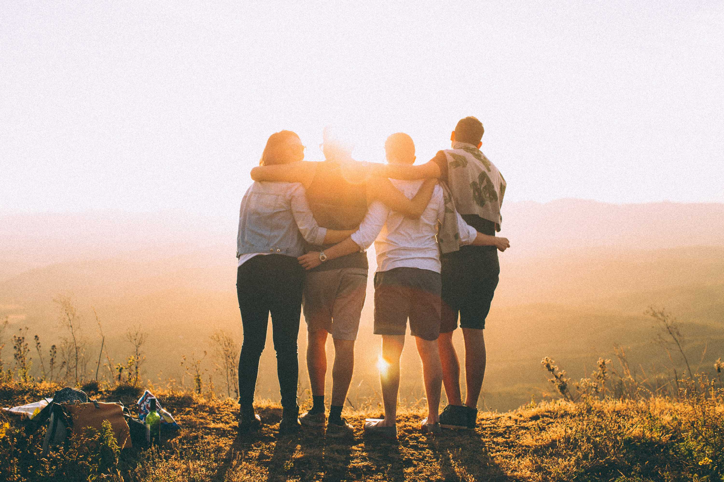 Four people embrace while watching the sunset for a story about how to enjoy the benefits of travel without going anywhere.