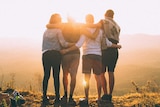 Four people embrace while watching the sunset for a story about how to enjoy the benefits of travel without going anywhere.
