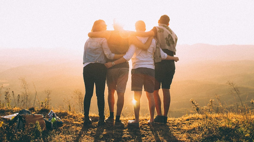 Four people embrace while watching the sunset for a story about how to enjoy the benefits of travel without going anywhere.