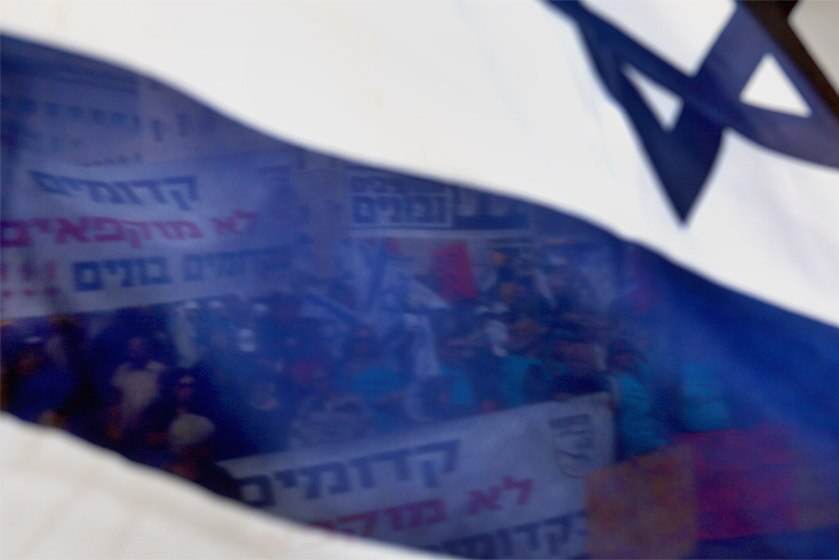 Right-wing Jewish settlers are seen through an Israeli flag as they protest outside Prime Minister Benjamin Netanyahu's officer