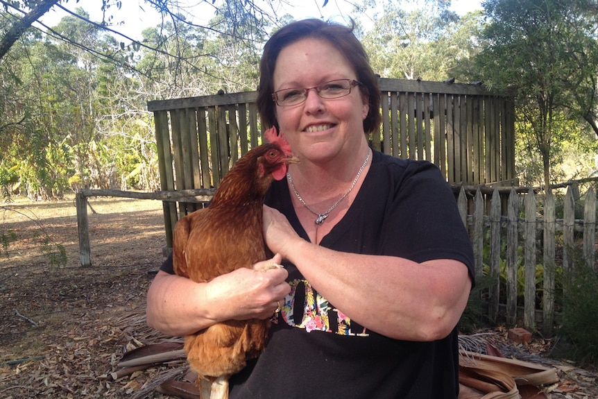 A smiling woman with dark hair cradles a chicken.