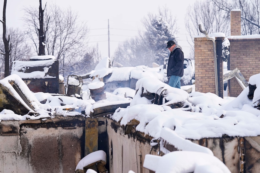 Daniel Peers looks through the snow covered remains of his brother's burned homes.