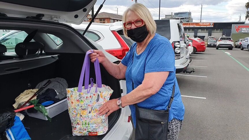 A masked woman loads a shopping bag into a car