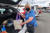 A masked woman loads a shopping bag into a car