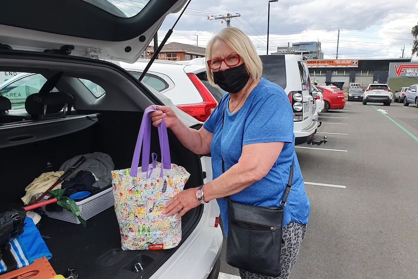 A masked woman loads a shopping bag into a car.