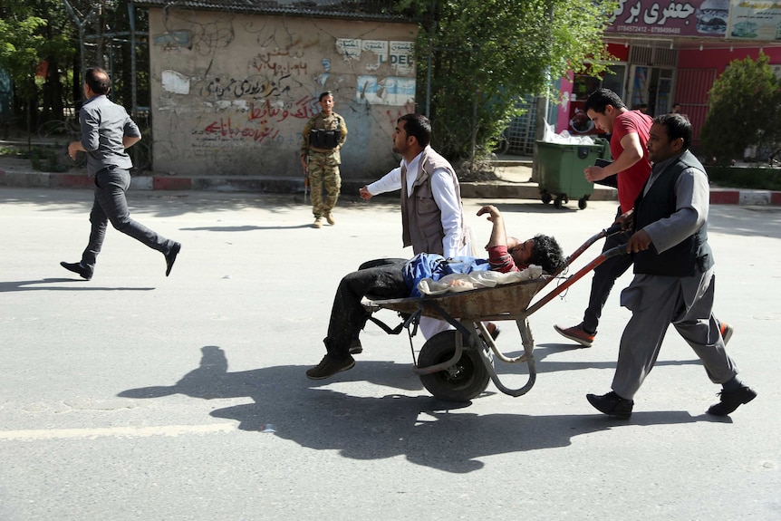Afghan men carries a wounded man in wheelbarrow