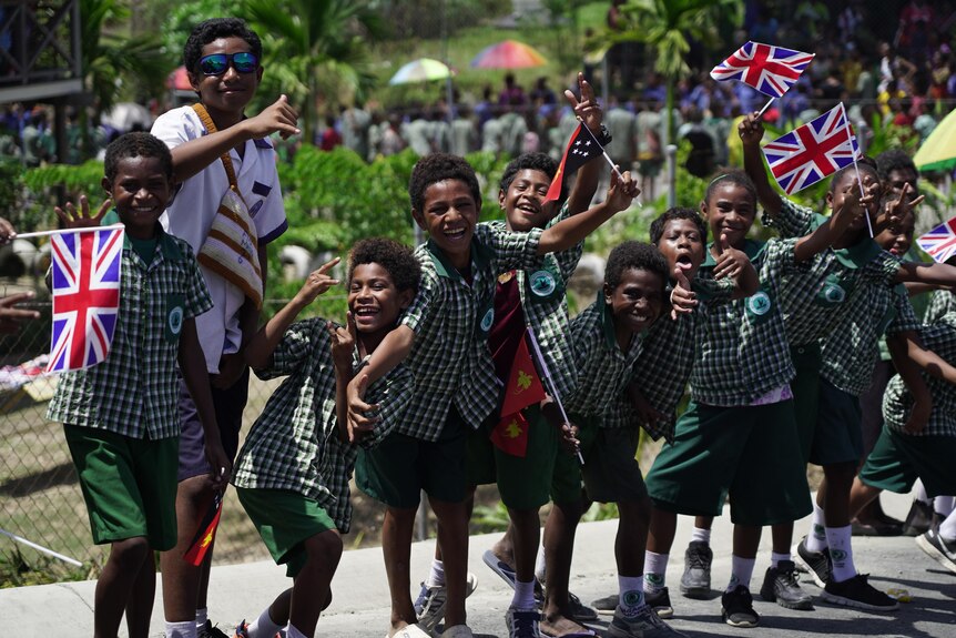 A group of Papua New Guinean children in school uniforms waving union jack flags