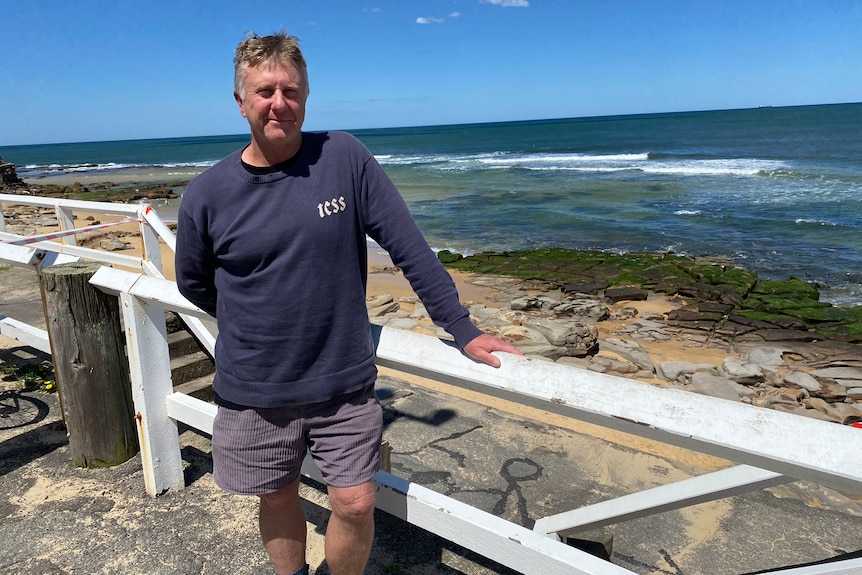 a man stands in front of a white barrier fence in front of a beach