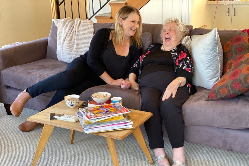 A younger woman and an older woman sit on the couch together, laughing.