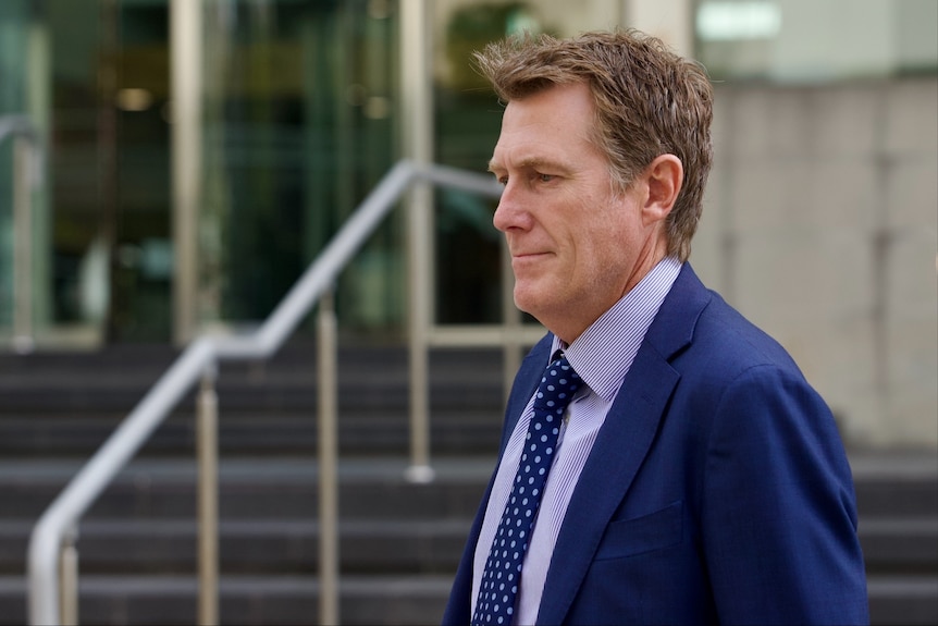 A side-on shot of Christian Porter wearing a suit and tie and smiling outside court in Perth.