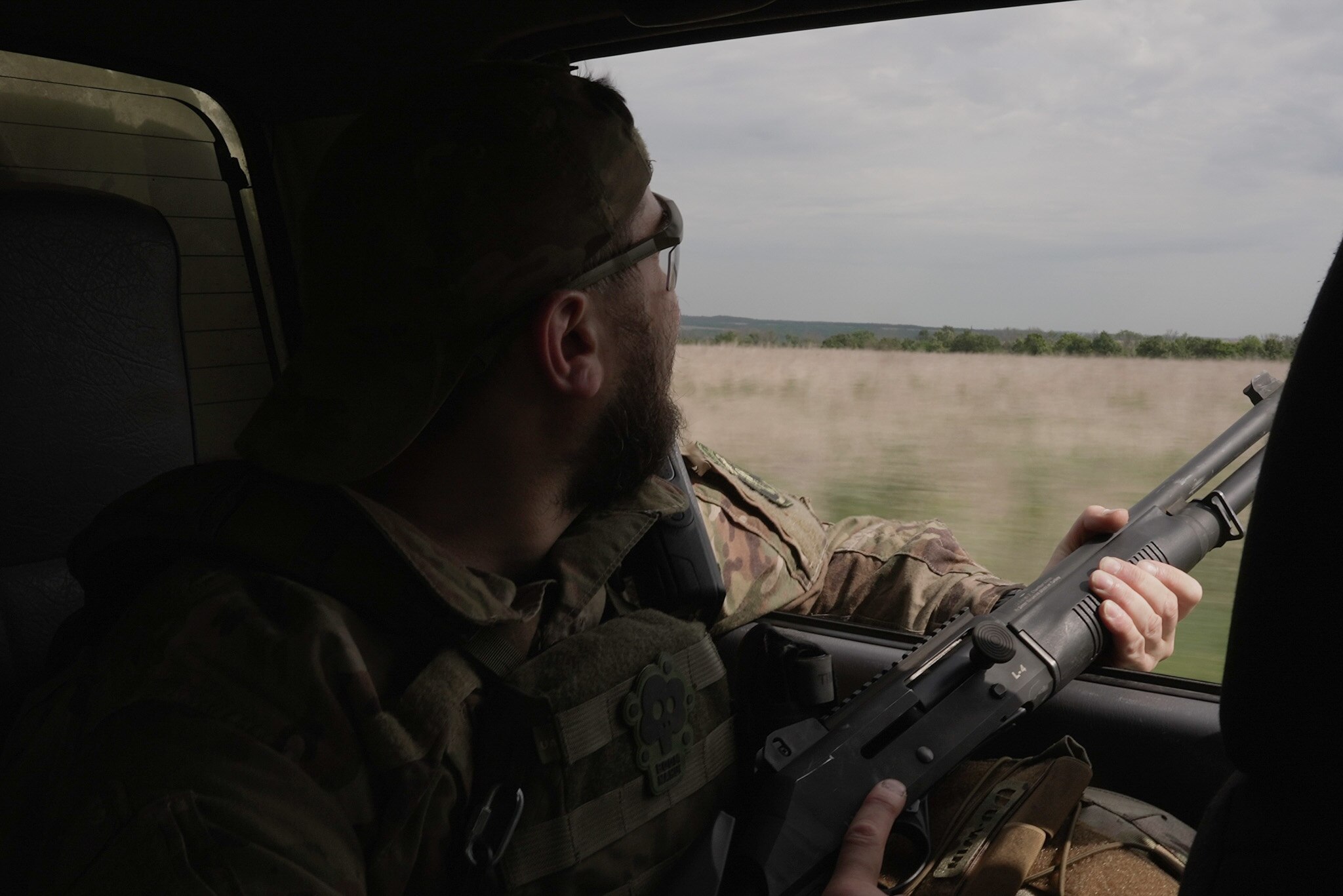 A soldier hold his gun out the window of a car.