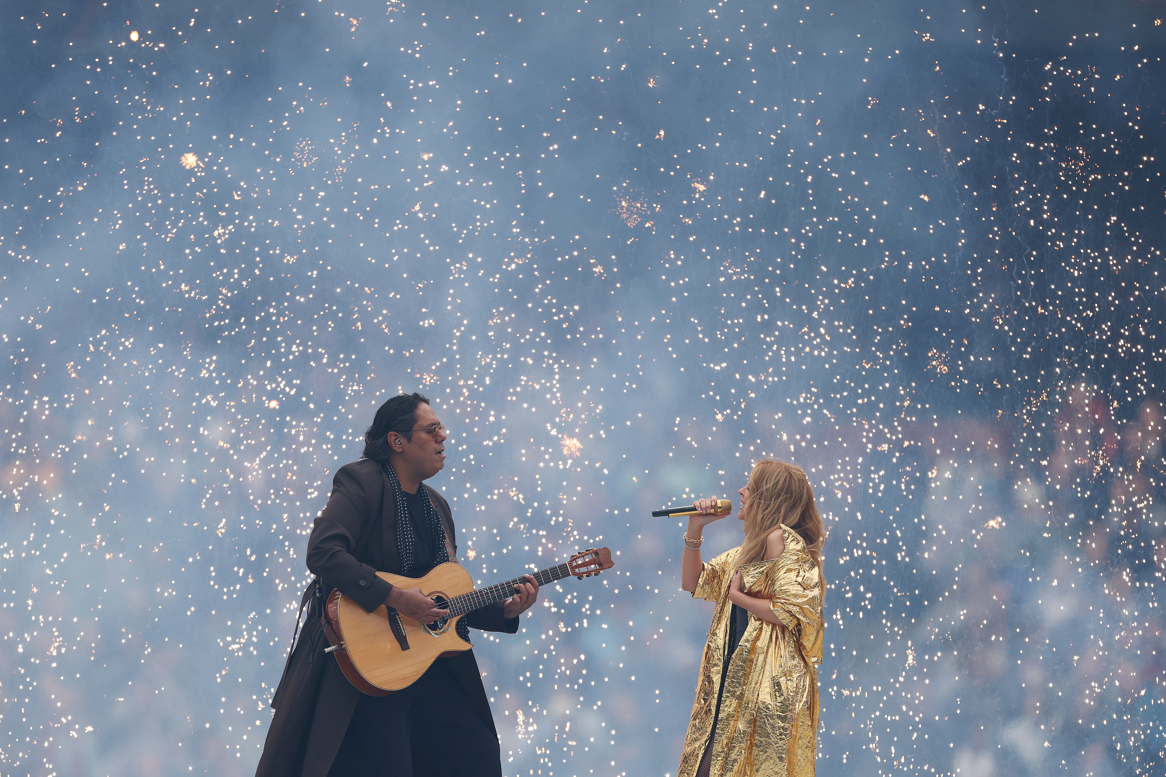 William Barton wearing a long black coat and Kylie Minogue in a metallic gold coat