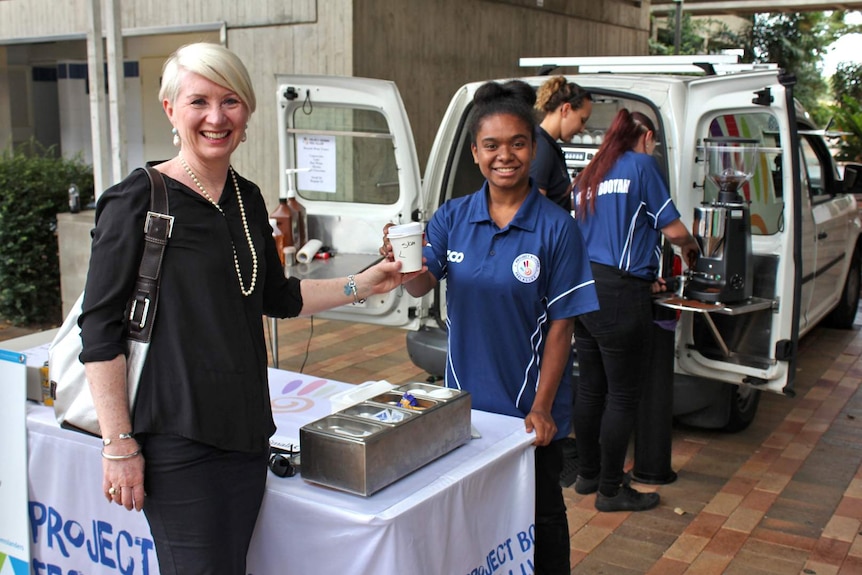 A teenage girl serves a woman coffee in a takeaway paper cup