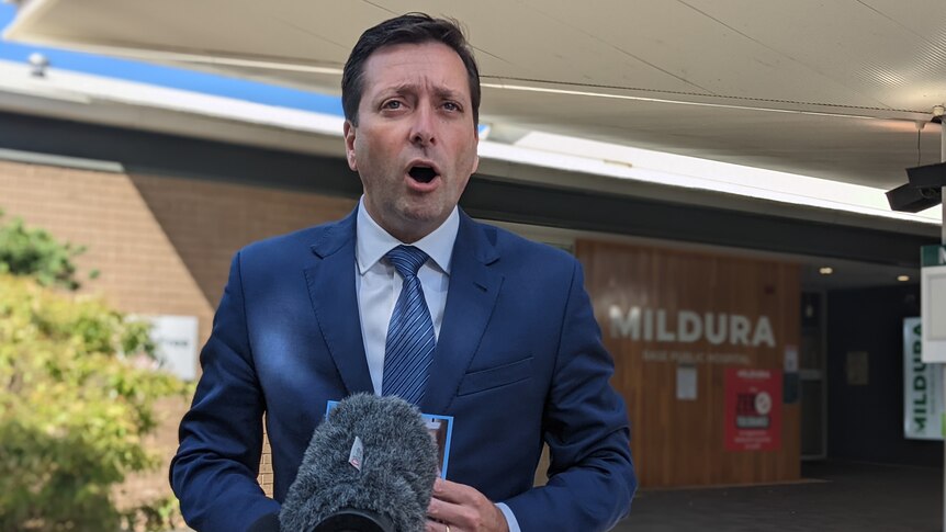 A man in a suit speaking at a press conference in front of hte Mildura Base Public Hospital. 