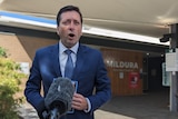 A man in a suit speaking at a press conference in front of hte Mildura Base Public Hospital. 