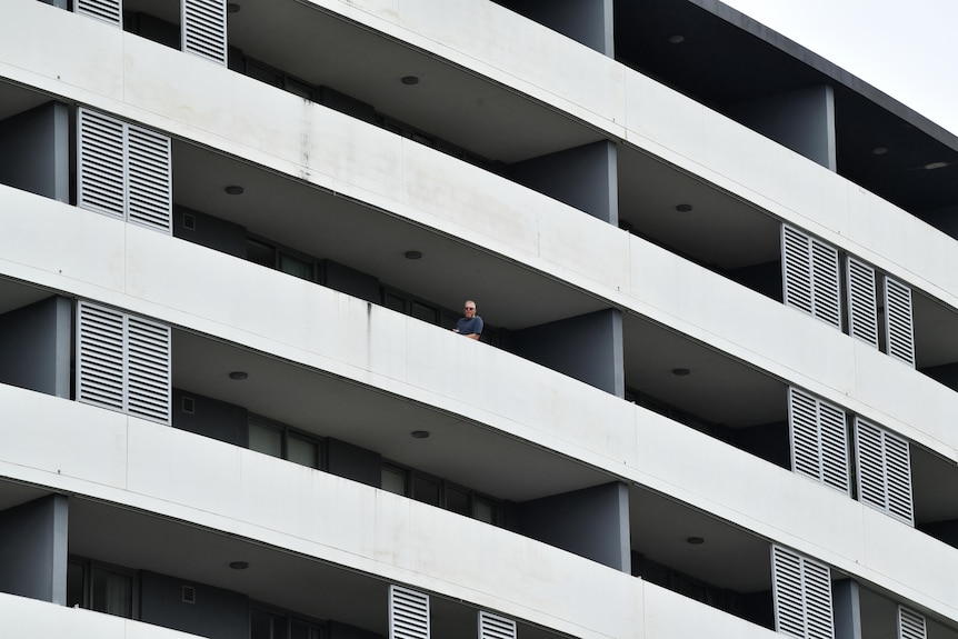 A man can be seen from the distance leaning over a long balcony on a multi-story building