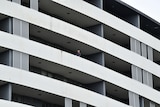 A man can be seen from the distance leaning over a long balcony on a multi-story building