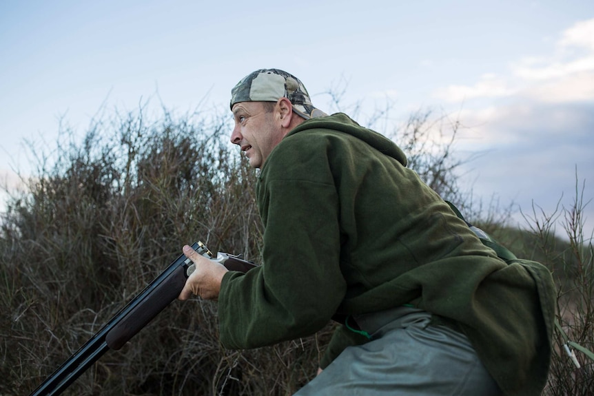 Duck hunter David Laird crouches amongst marsh grass in an attempt to camouflage himself.