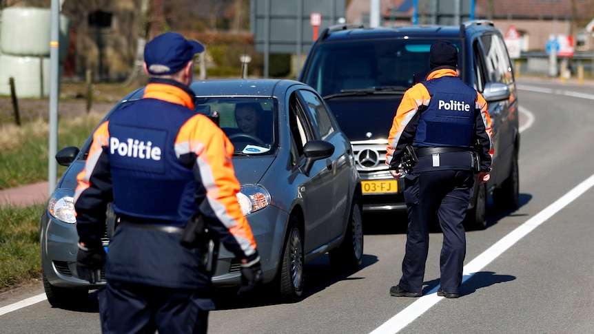 Image of two Belgian police officers walking up to two cars that have been stopped. On their back white letters with 'politie'.