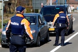 Image of two Belgian police officers walking up to two cars that have been stopped. On their back white letters with 'politie'.