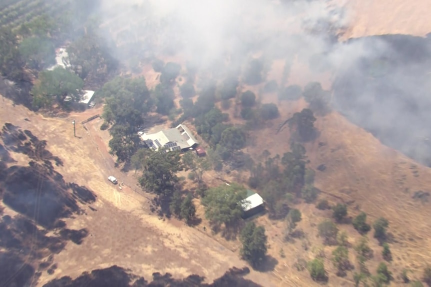 An aerial of a house with smoke billowing from a nearby bushfire.