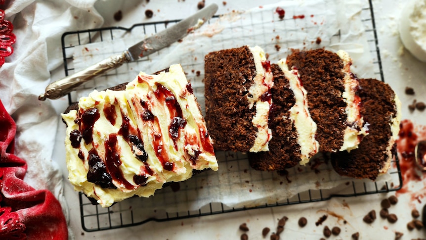 Ella Rossanis' chocolate cherry loaf with sour cream icing on a baking tray, with four slices laying on their side.