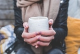 A woman puts her hands around a coffee cup. She is wearing a jacket and scarf.